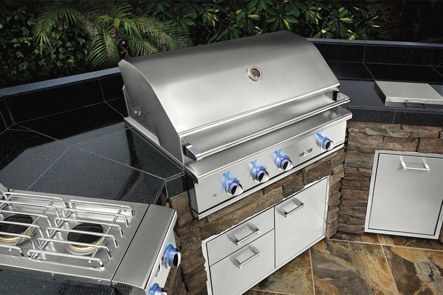 A grill with blue knobs and a stone wall.